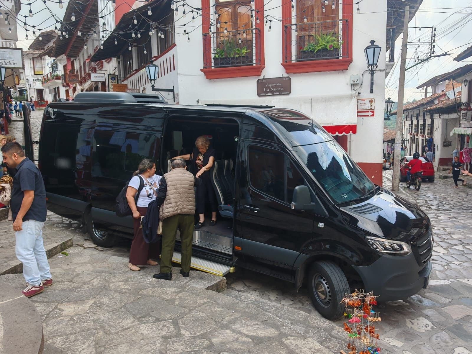 Pasajeros de un grupo descendiendo de una Mercedes-Benz Sprinter negra en la calle empedrada de un pueblo